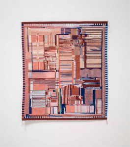 A photograph of Replica of a Chip by Marilou Schultz, a woven geometric piece hanging on a white wall.